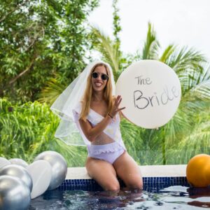 Smiling bride in a bikini holding a balloon, enjoying a poolside celebration.