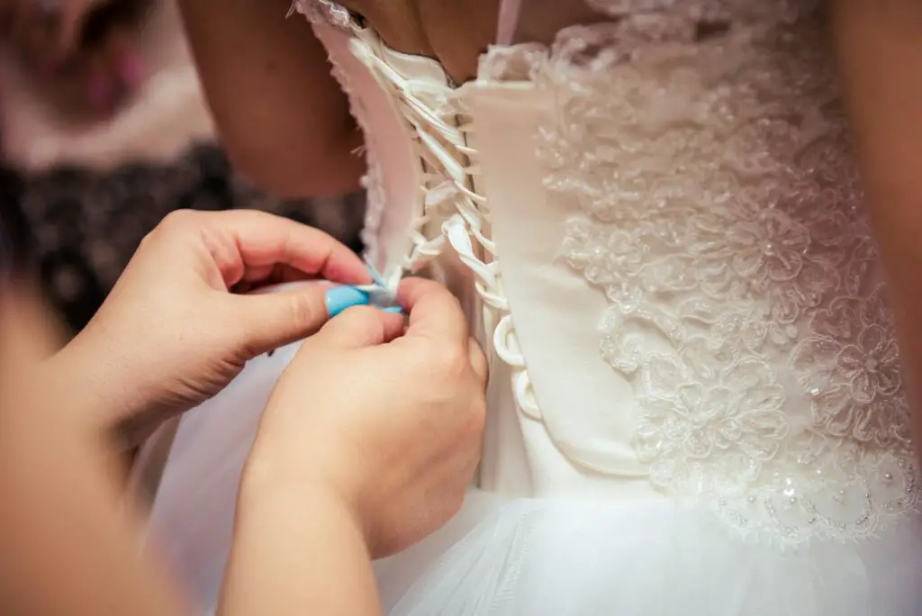 Detailed image of hands lacing a beautiful bridal gown, showcasing elegant wedding preparation.
