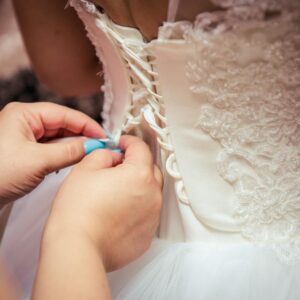 Detailed image of hands lacing a beautiful bridal gown, showcasing elegant wedding preparation.