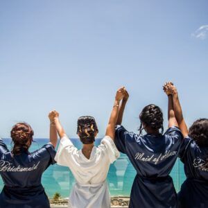 A joyful bridal party with friends in robes celebrates an oceanfront view, creating a memorable pre-wedding moment.