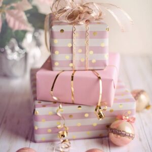 Charming Christmas presents wrapped in pink and gold with festive ornaments on a wooden table.