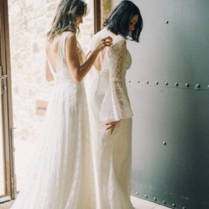 Two brides sharing a tender moment in elegant white dresses by a doorway.